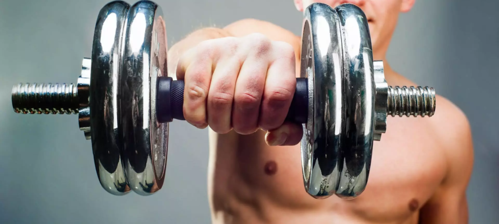 hombre con torso al descubierto eleva frontalmente una mancuerna con su brazo derecho