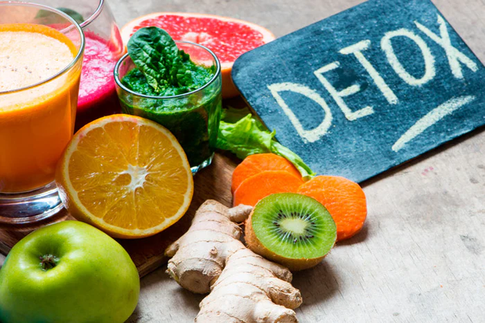 frutas variadas y licuados de hortalizas expuestas sobre un tablero haciendo alusión a la palabra detox en mayúsculas