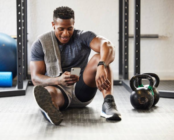 hombre de color sentado en el gimnasio observando su móvil