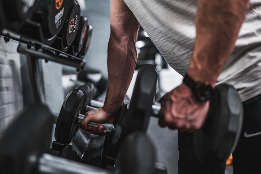 hombre coge de un soporte de pesas dos mancuernas en un gimnasio