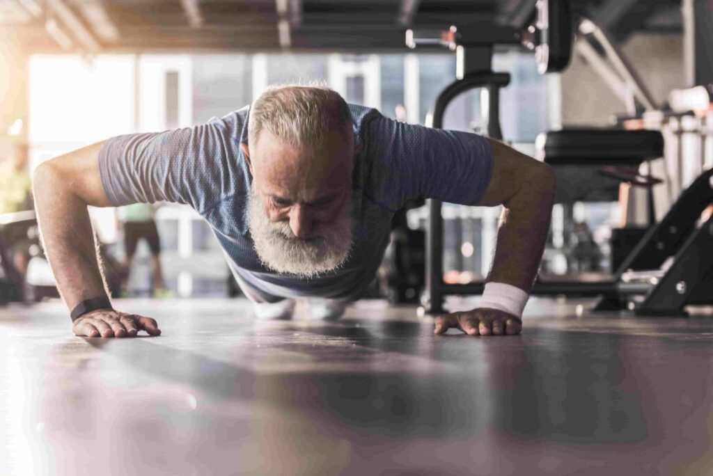 cliente avanzado en edad con barba blanca realiza flexiones en el suelo en un gimnasio