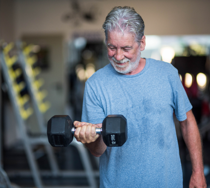 hombre de avanzada edad coge una mancuerna con su mano y levanta esta con la fuerza de su brazo derecho