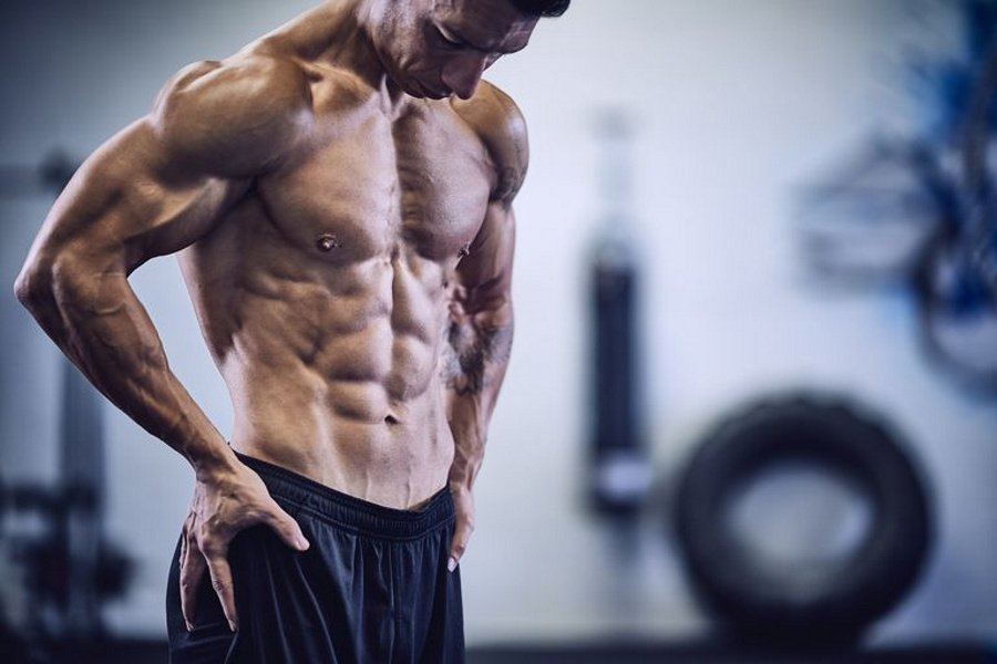 hombre con edad superior a los 40 años musculado y definido muestra su torso apoyando sus manos sobre la cintura e inclinando ligeramente la cabeza hacia abajo