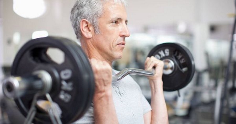 hombre de mas de 45 años haciendo un curl de bíceps con barra