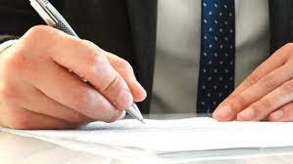 dedos de un mano aparecen escribiendo sobre papel con una pluma